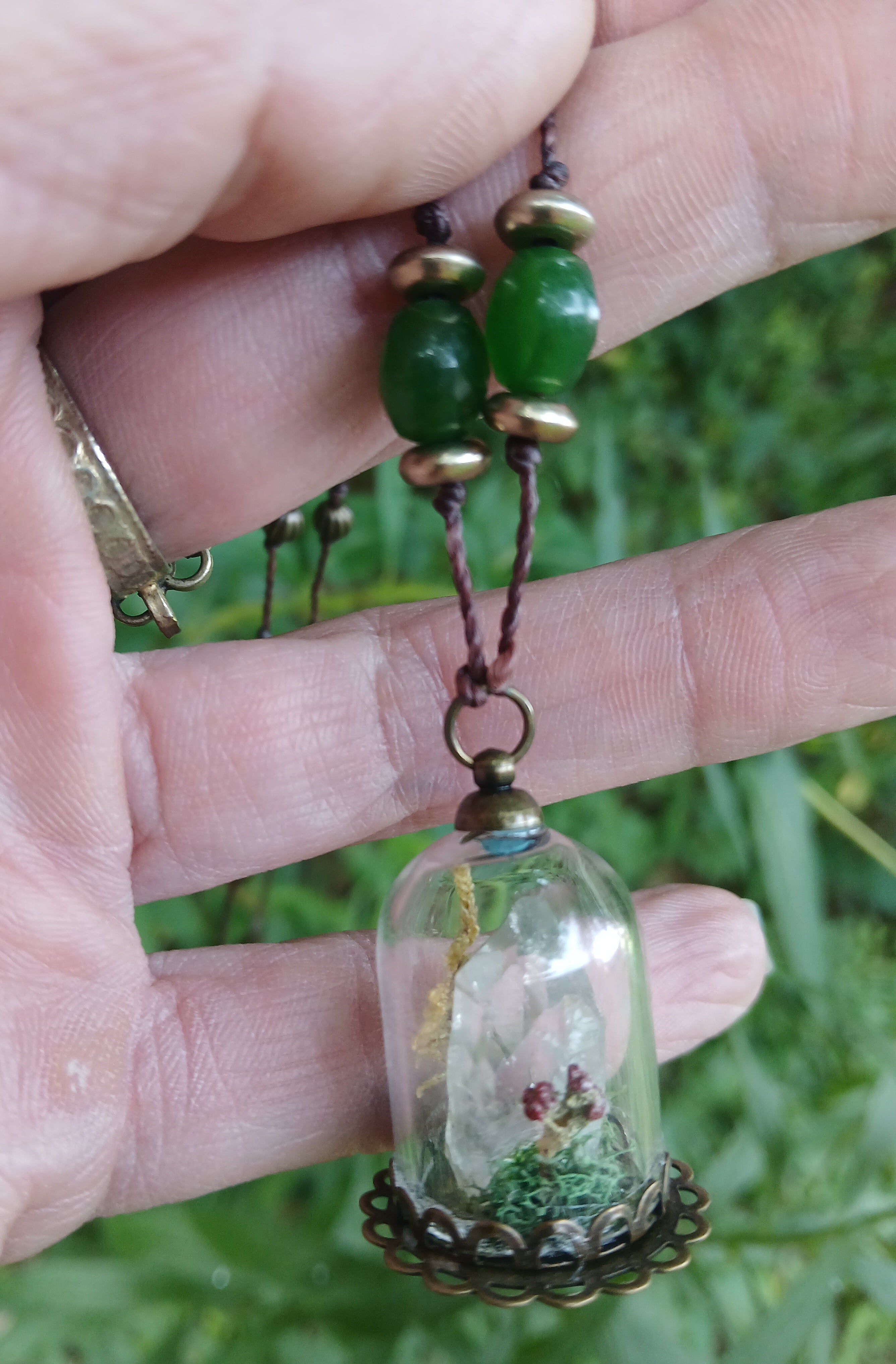 Close view of the quartz and moss terrarium pendant held in hand