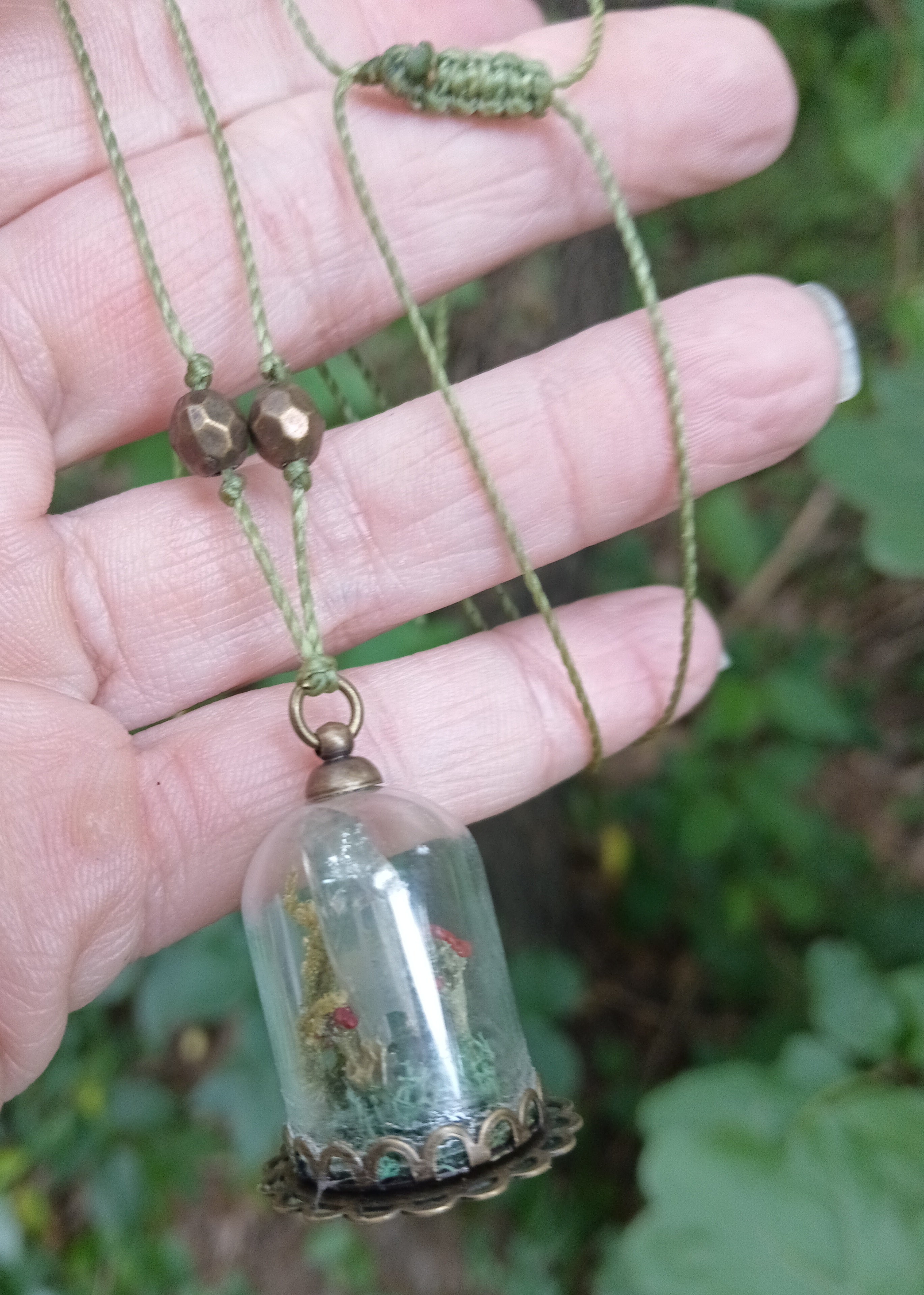 Glass cloche pendant with red toadstools and moss on olive cord with brass beads