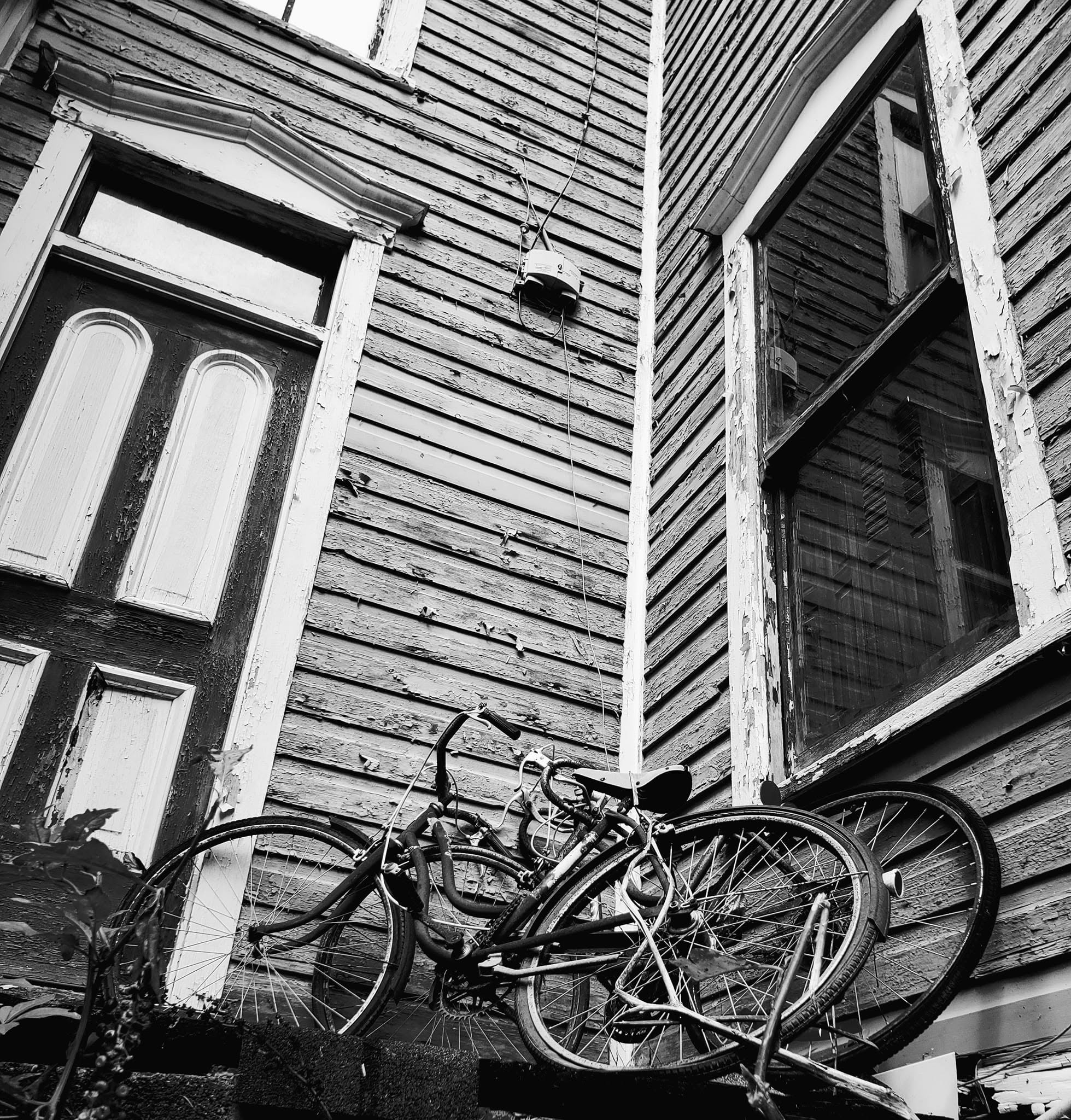 Black and white photograph of two old bicycles against a weathered clapboard house